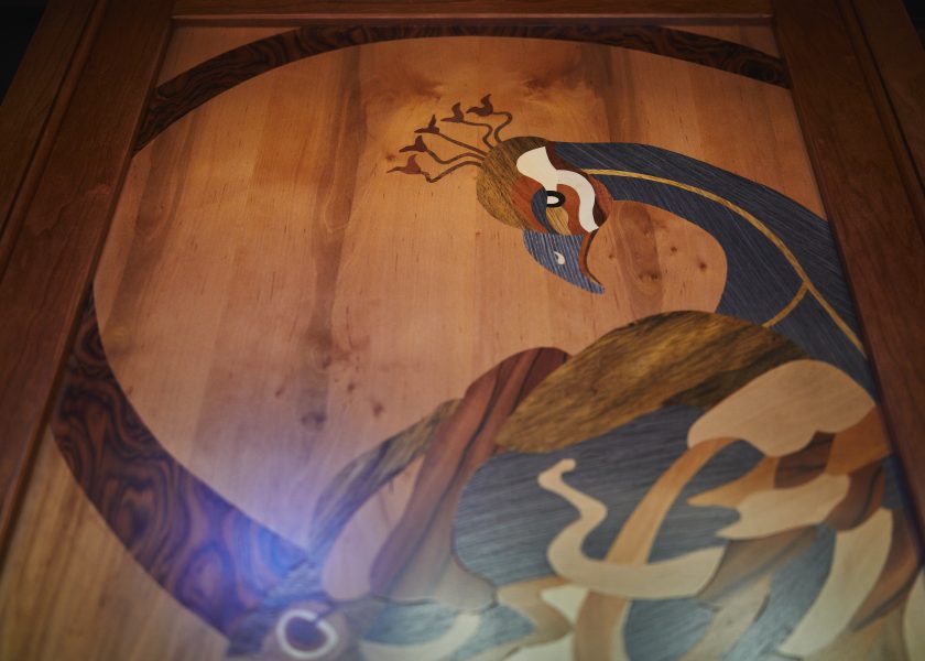 Close-up of a cabinet door depicting a peacock, the peacock made by marquetry.