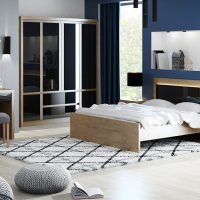 The visualisation shows a bedroom with furniture from the Andre collection, modern furniture, simple geometric shape, oak lefkas plus black gloss. The picture shows a dressing table with a pouffe, a bed with bedside tables and a large wardrobe divided into smaller cabinets and drawers.