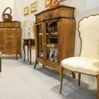 A photo from the stand at the 2020 Furniture Poland Fair. The photo shows an upholstered stylish chair, a stylish wooden display case and a wooden chest of drawers.
