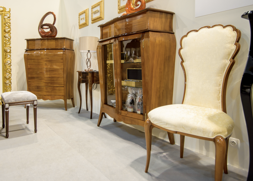 A photo from the stand at the 2020 Furniture Poland Fair. The photo shows an upholstered stylish chair, a stylish wooden display case and a wooden chest of drawers.
