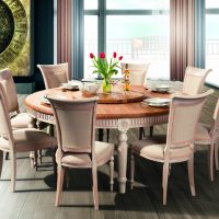 Classic round wooden table with decorated legs together with a set of chairs in light upholstery.
