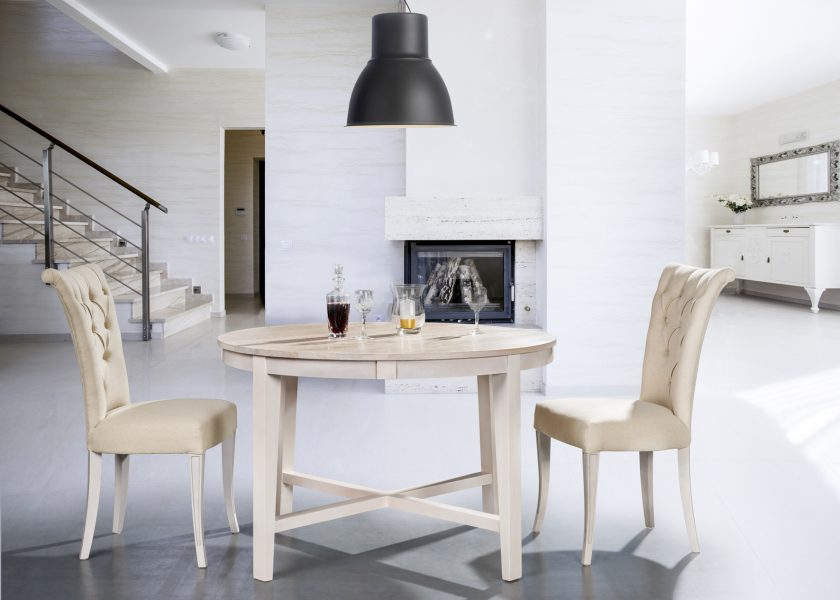 Wnętrze salonu, drewniany stół oraz dwa drewniane krzesła z jasną tapicerką.